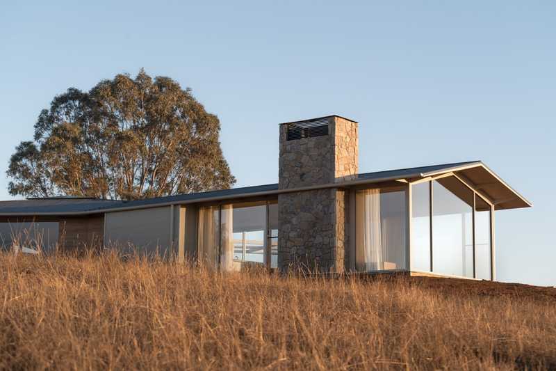 A frame of an external view of Table Top House with large fixed pane windows that provide views over Lake Hume.